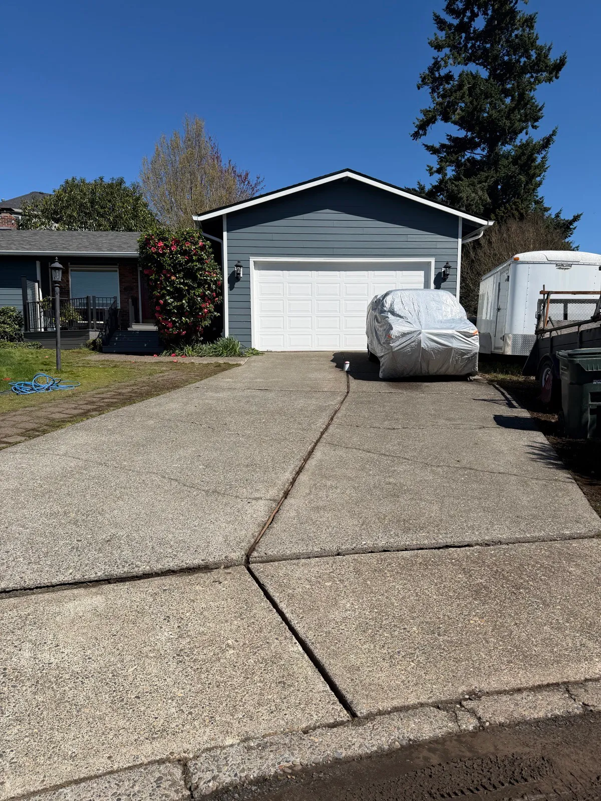 Concrete driveway freshly pressure washed, moss gone, leading up to a blue garage