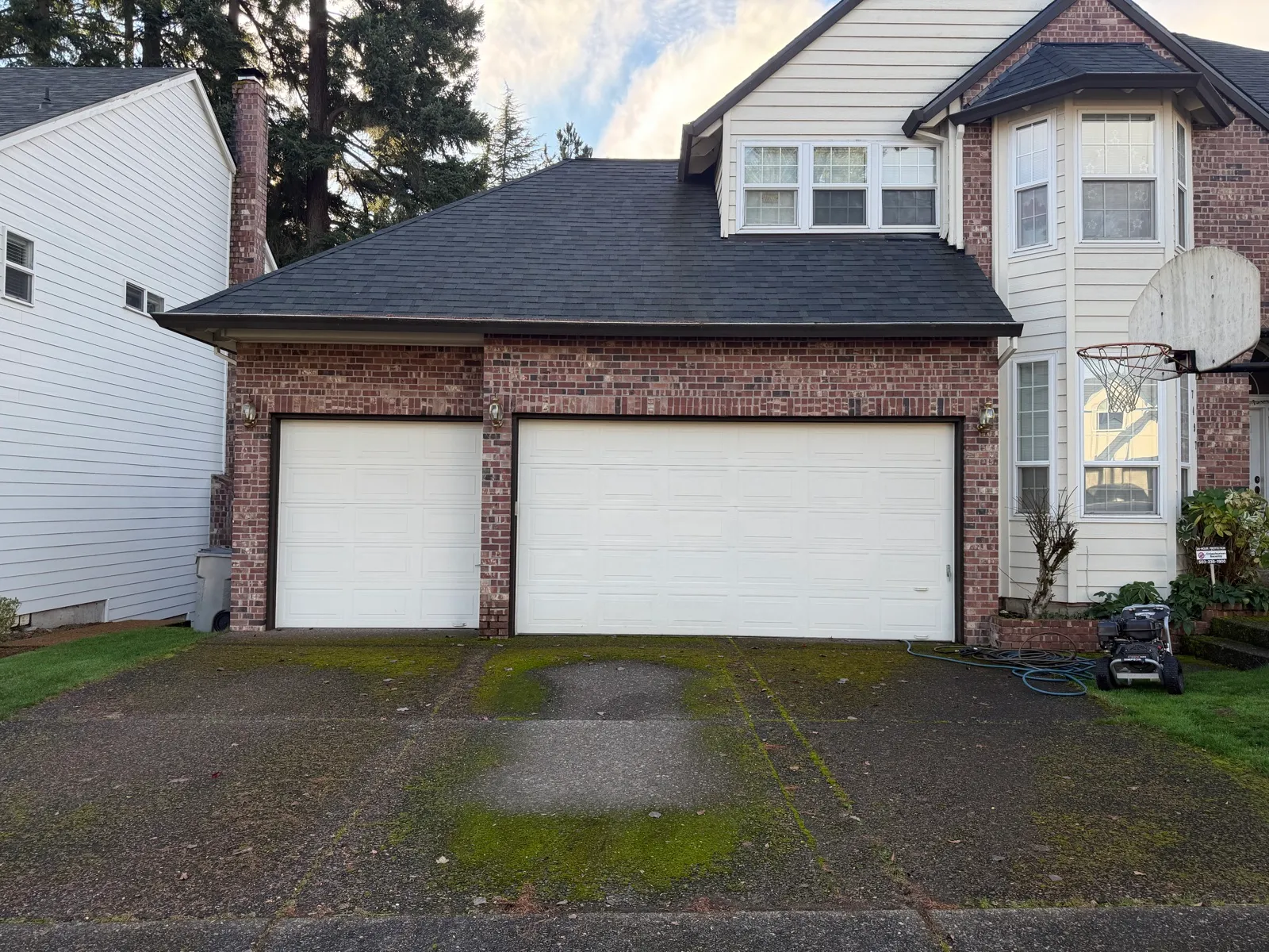Before: concrete driveway at a brick garage with moss lines and a clean test strip