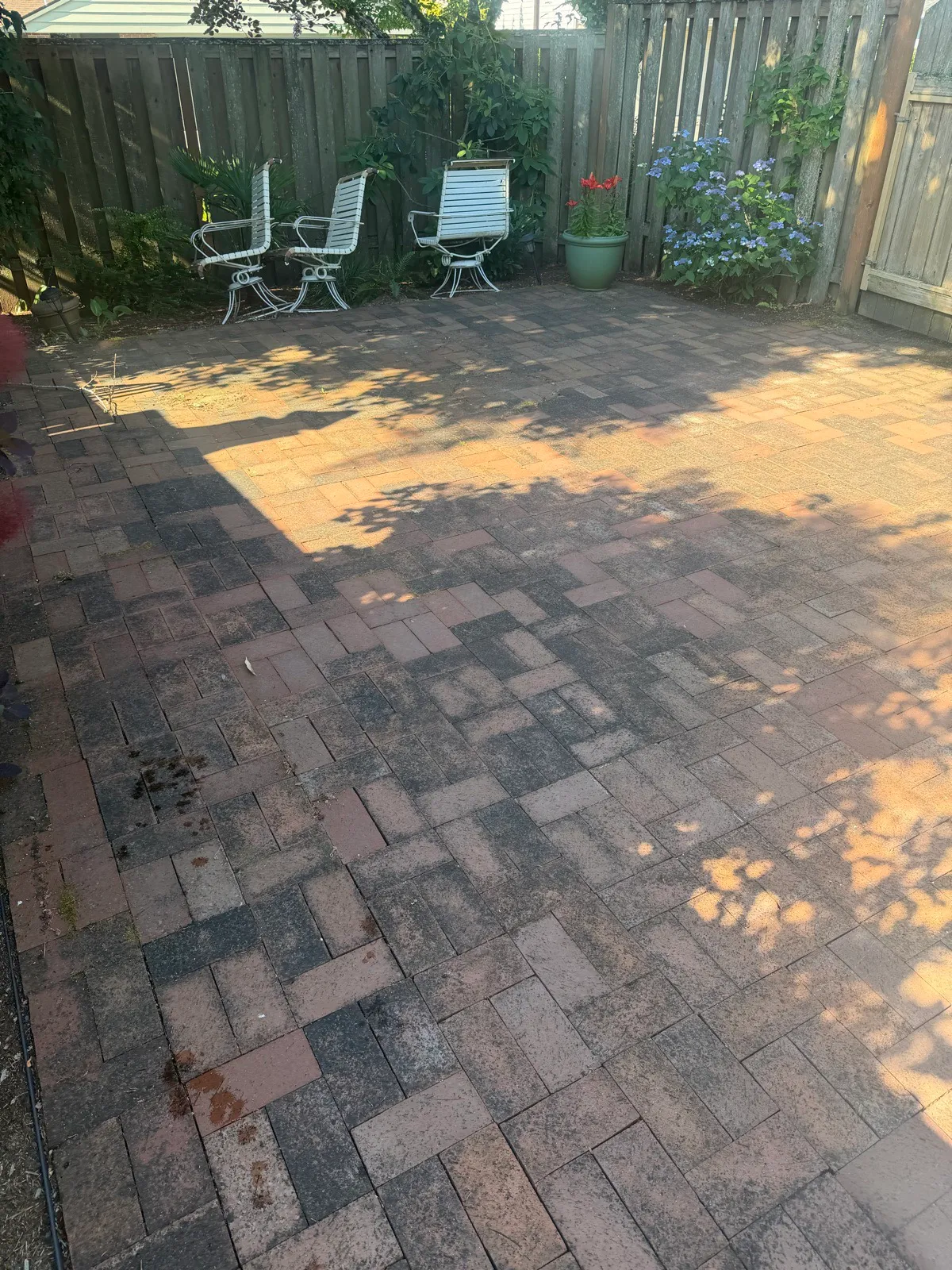 Before: brick paver patio blackened with grime, garden chairs against the fence