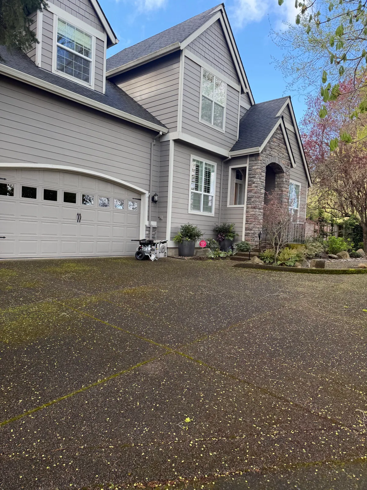 Before: exposed-aggregate driveway lined with moss in front of a craftsman garage